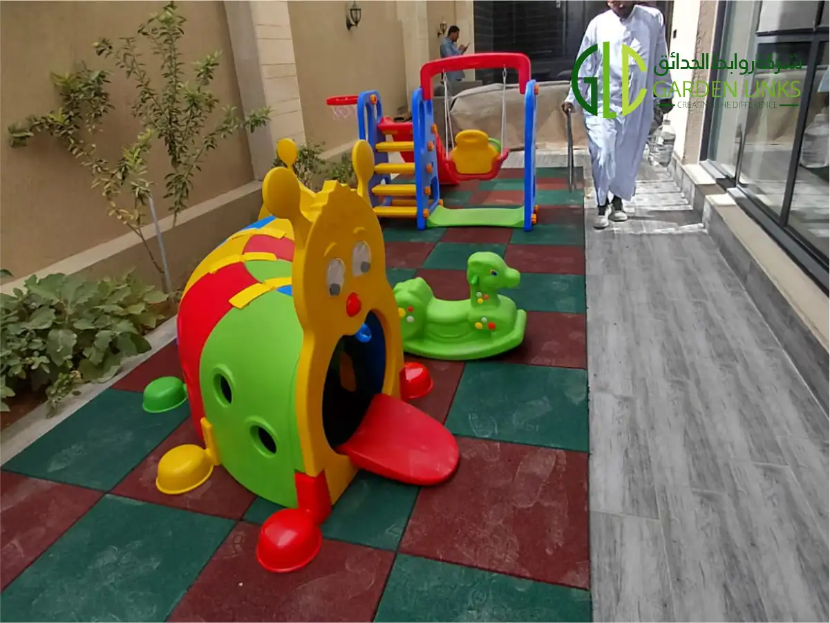 Colorful outdoor playground equipment including slides, swings, artificial grass, and rubber safety tiles installed at a residential house in Riyadh.