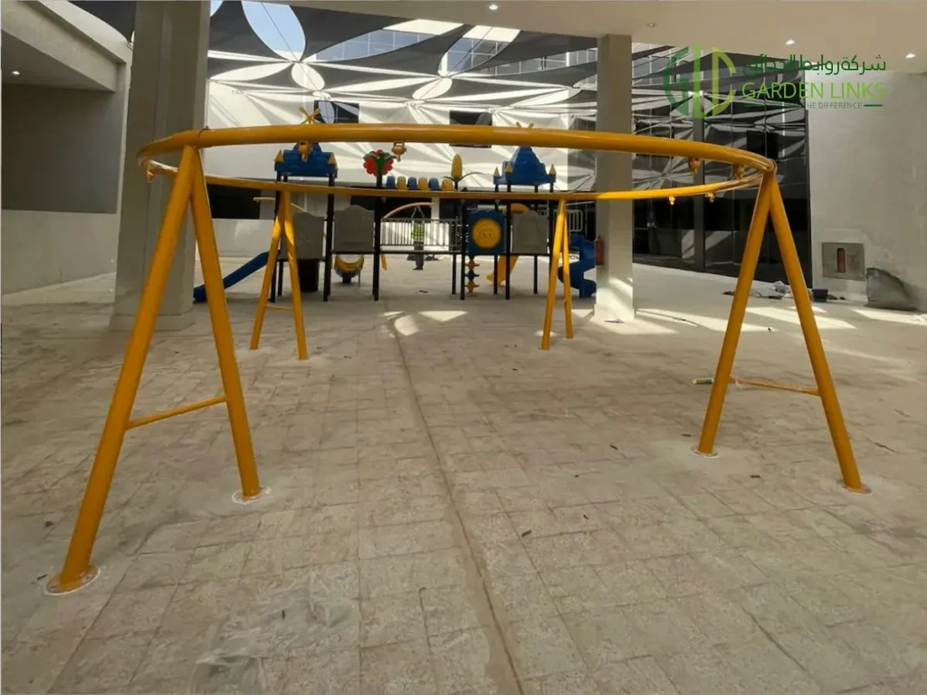 Yellow circular swing frame installed in Makkah covered courtyard playground equipment project with tiled flooring, shade sail coverage, and fixed base plates