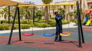 Maintenance technician inspecting swing chains, suspension bearings, hooks, seat condition, and frame connections in a Saudi playground