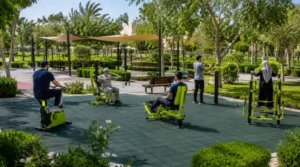 Compact six-machine outdoor fitness area in a Saudi neighbourhood park with rubber flooring and shaded seating