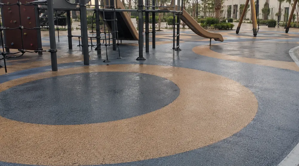 Well-drained rubber playground flooring with clean channels and protected metal equipment in a coastal Saudi setting