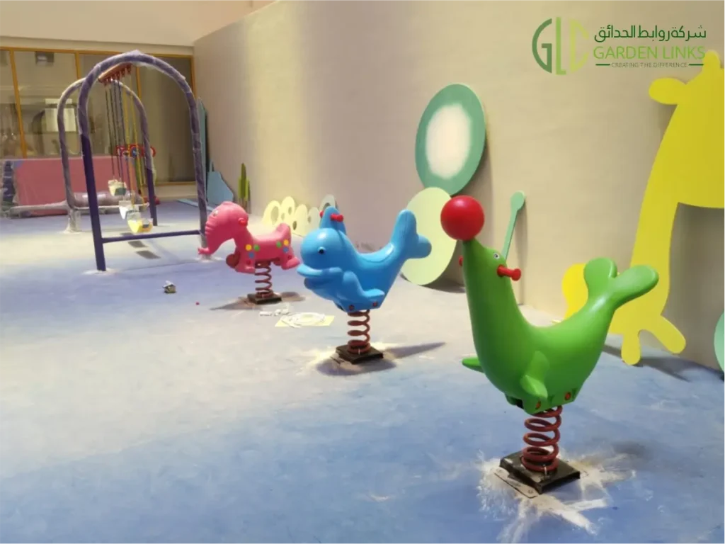 Indoor playground area featuring colorful animal-shaped spring riders, a children’s swing set, and nature-themed wall decorations.