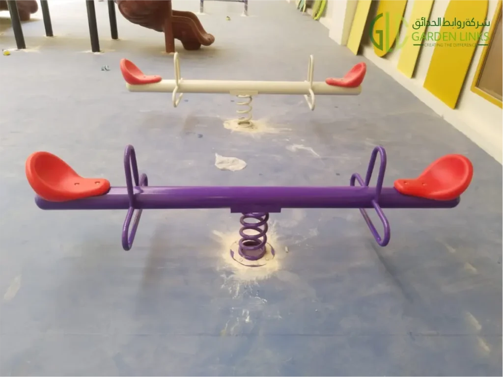 Colorful indoor playground seesaws with red seats and spring-mounted bases, installed in a children’s play area.