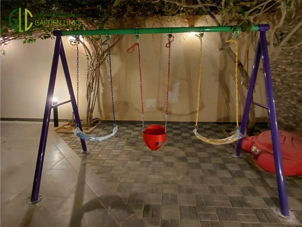 Close-up of a purple swing frame with colored chains and safety seats on rubber paver flooring in a Saudi villa