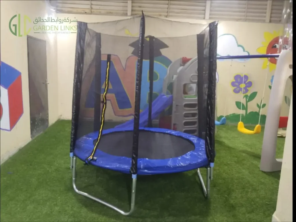 Indoor trampoline with protective safety net installed over artificial grass at a school play area in Riyadh.