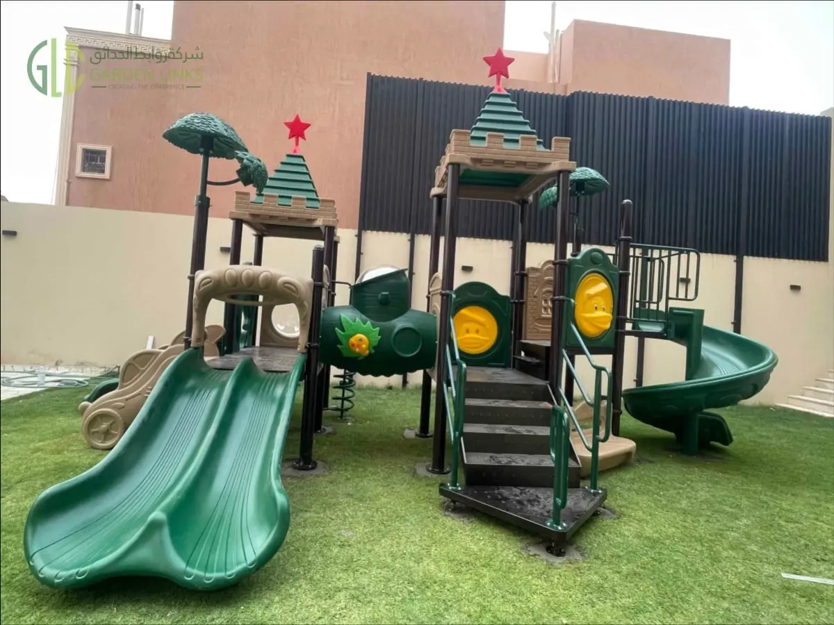 Outdoor school playground equipment in Riyadh with green double slide, spiral slide, access stairs, themed play towers, safety rails, and artificial grass.