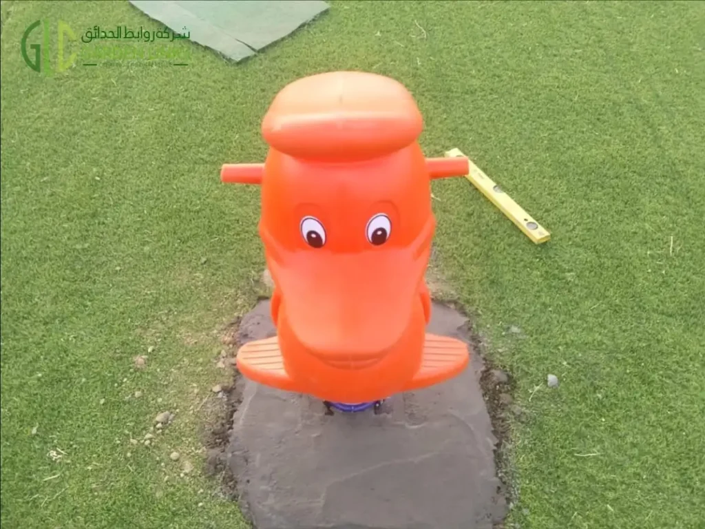 Orange animal-themed spring rider installed on artificial grass at a public park playground in Madinah.