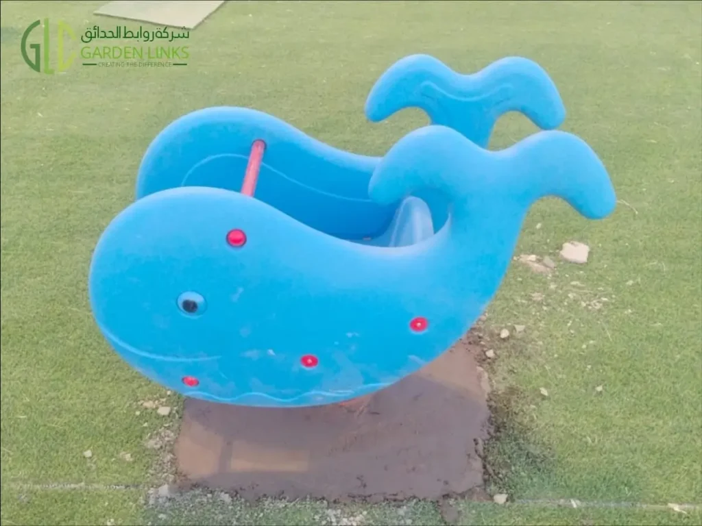 Blue whale-themed playground rocker installed on artificial grass at a public park playground in Madinah.
