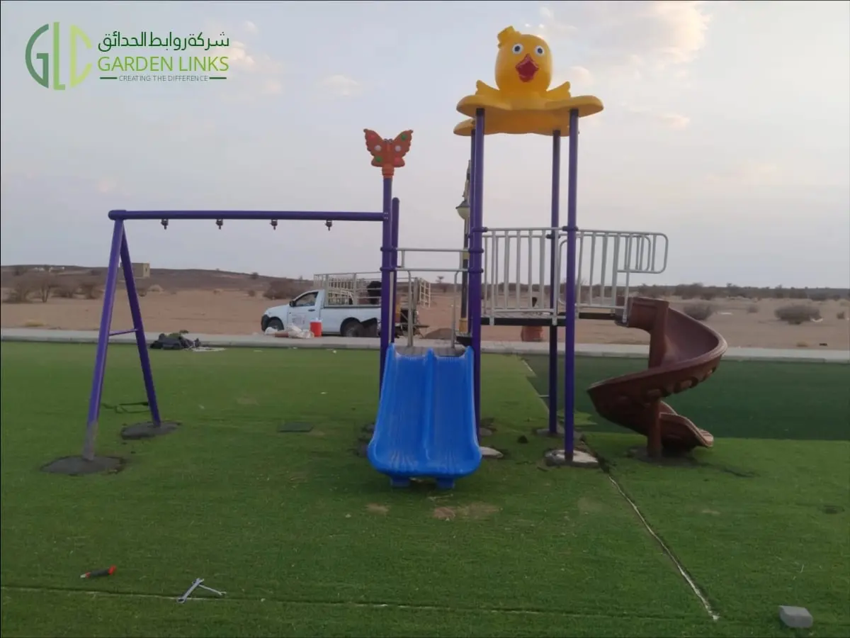 Multi-activity playground structure installed in a Madinah public park with blue straight slide, brown spiral slide, elevated platform and swing frame.