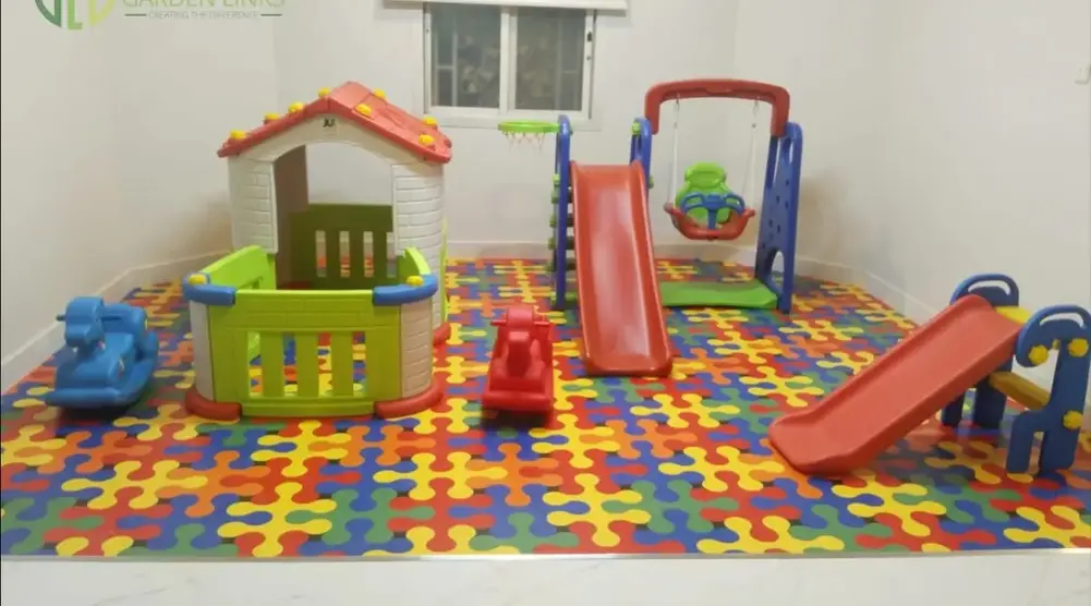 Indoor soft play area with toddler playhouse, slides, swing, rocking toys and colorful padded safety flooring.