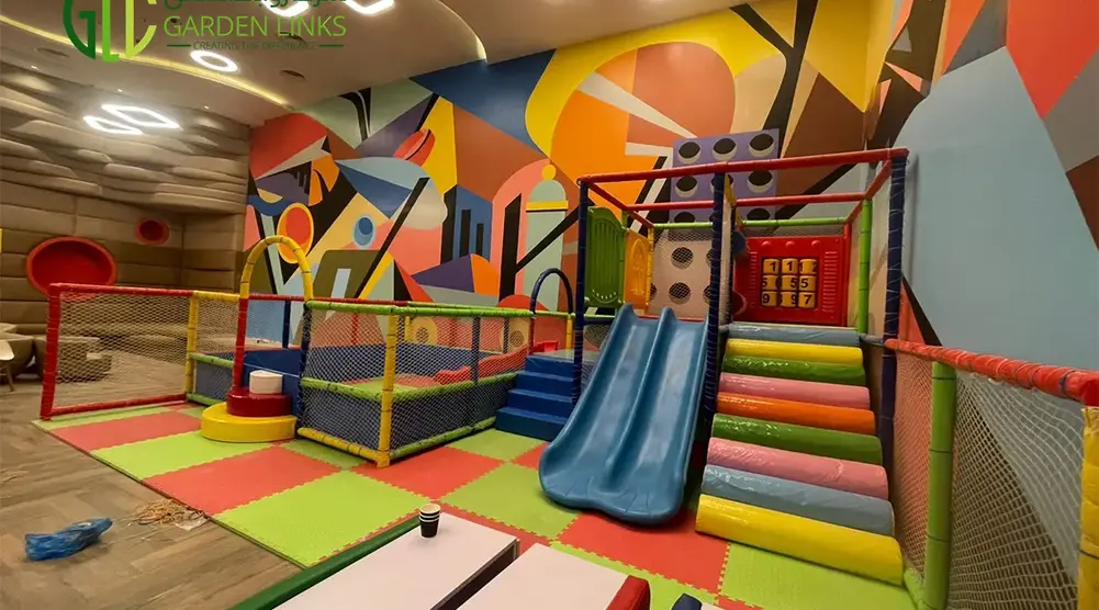 Indoor soft play area with double slide, padded stairs, safety netting, trampoline zone and colorful cushioned flooring.