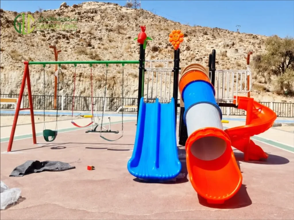 Children’s playground with tube slide, double slide, spiral slide and swing set installed in a public park in Taala, Saudi Arabia.