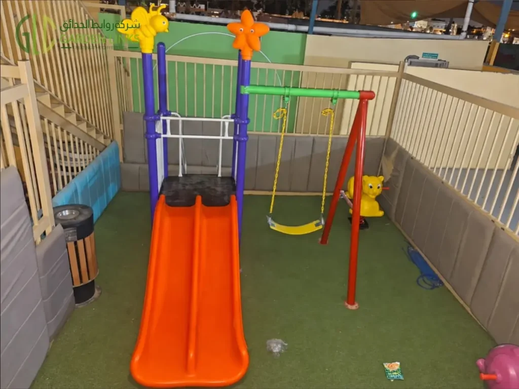 School playground installation in Najran featuring an elevated platform, double straight slide, single swing and artificial grass flooring.
