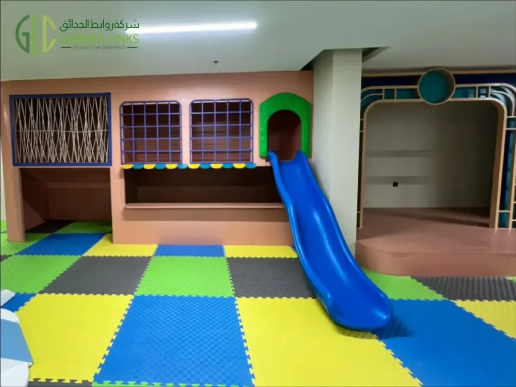 Indoor play structure with a blue slide, elevated platform, mesh barriers and colorful foam flooring.