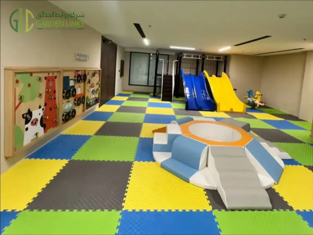 Wide view of an indoor play area with a circular soft-play set, wall activity panels and blue and yellow slides.