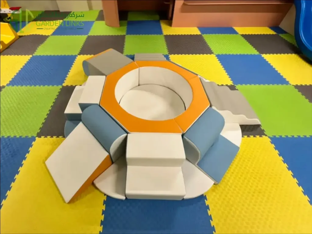 Circular soft-play set with a padded central opening, steps and ramps on colorful foam flooring.