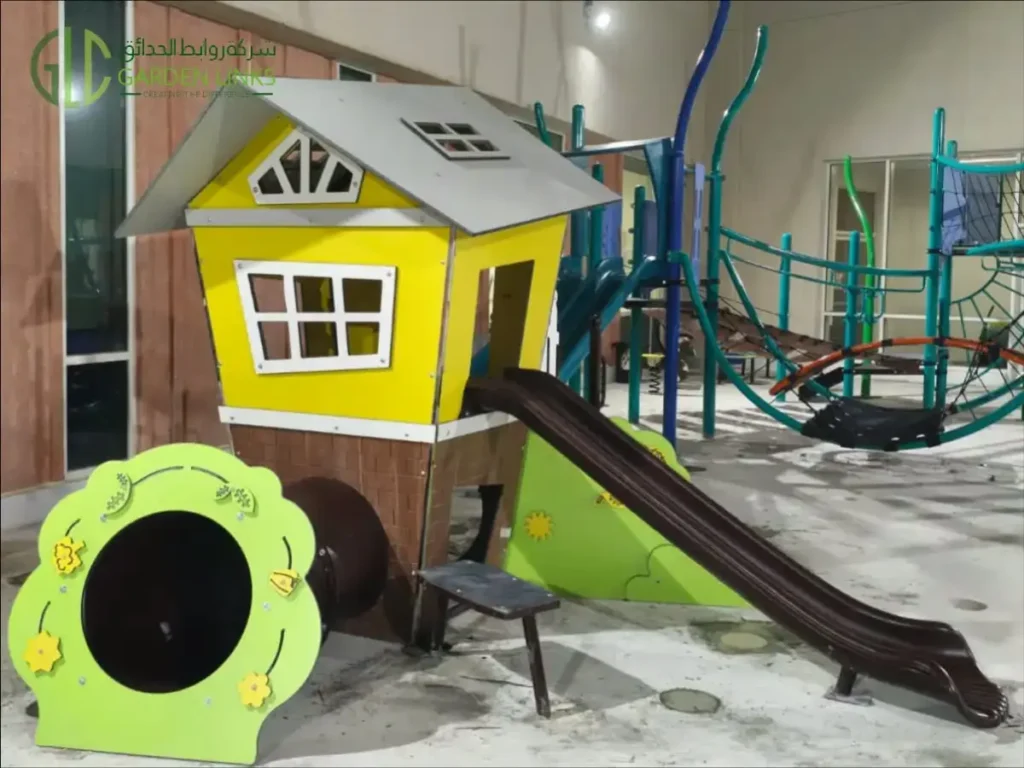 Aramco School Playground Al Ahsa yellow playhouse with a grey pitched roof, brown slide and low-level crawling opening.