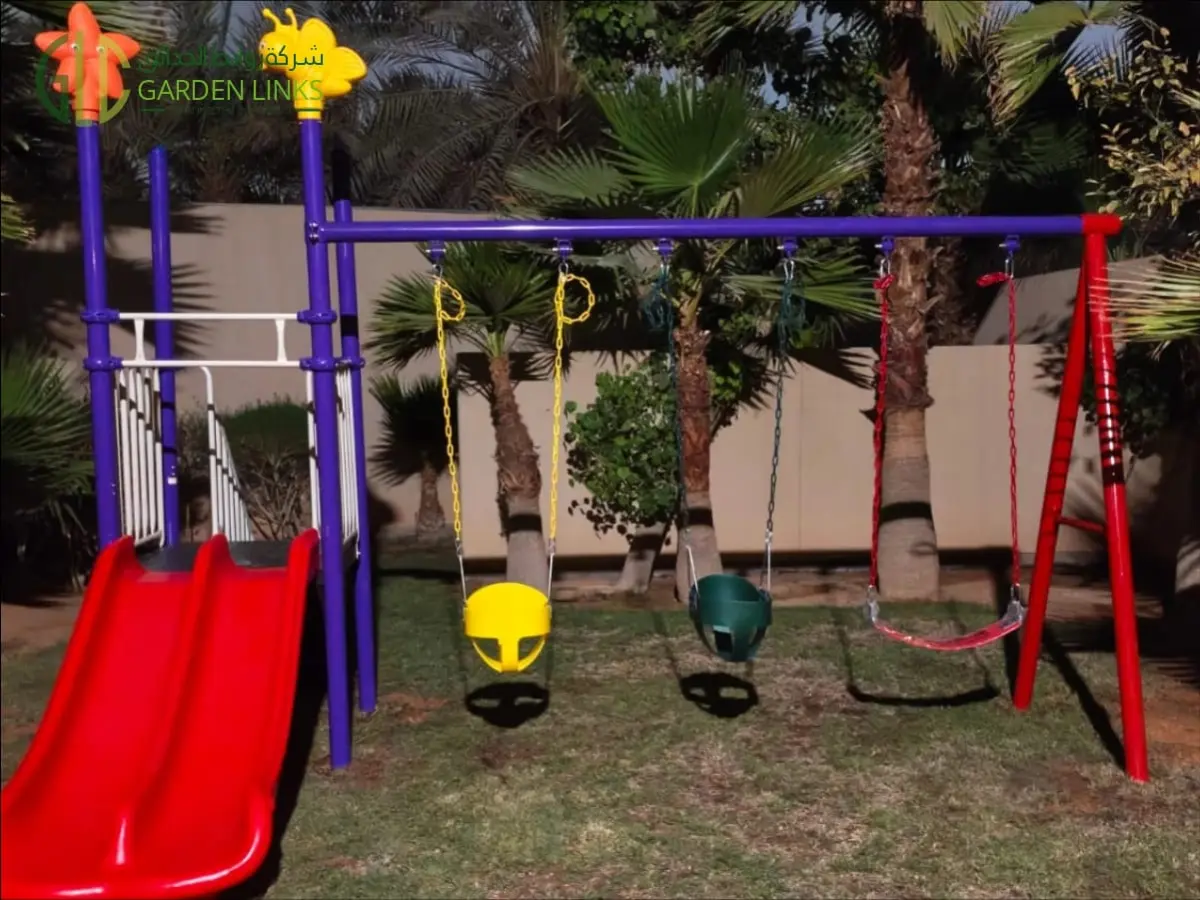 Home playset installation in Al Narjis with a red double slide, three swings, a raised platform and white railings in a palm-lined garden.