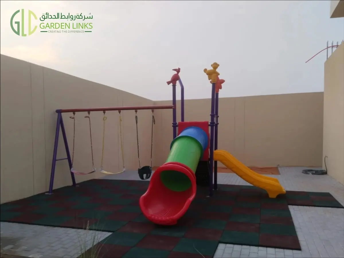Double and tube slide home playset in Riyadh with a red tube slide exit, yellow double slide, three swings and red and green safety flooring.