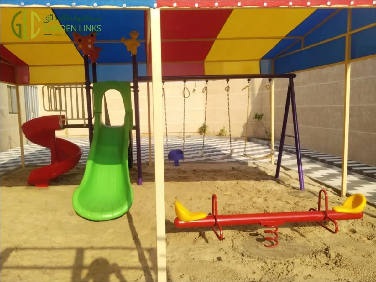 Shaded playset and seesaw installation in Banban with straight and spiral slides, three swings and a two-seat seesaw under a multicoloured canopy.