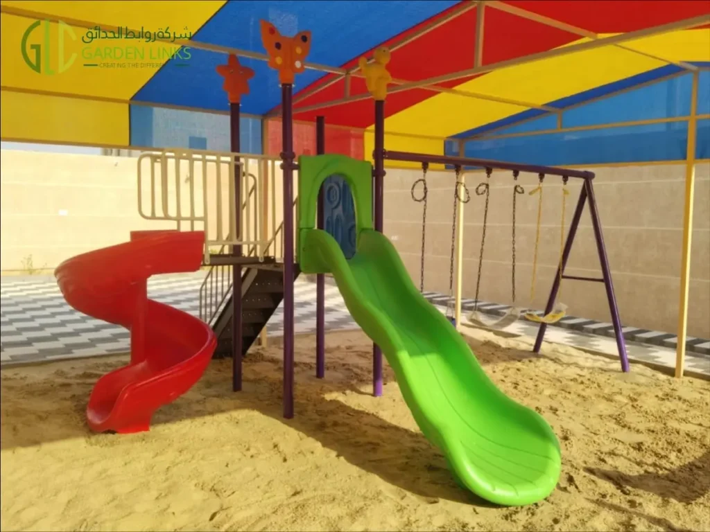 Green straight slide and red spiral slide connected to a raised platform at the shaded playset and seesaw installation in Banban.