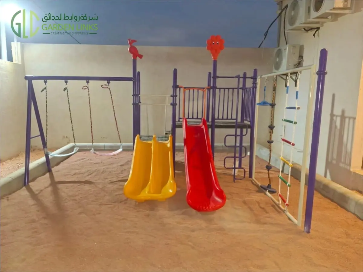 Front view of the two-swing climbing playset installation in Qiddiya City showing a yellow double slide, red straight slide and climbing rope with footholds.